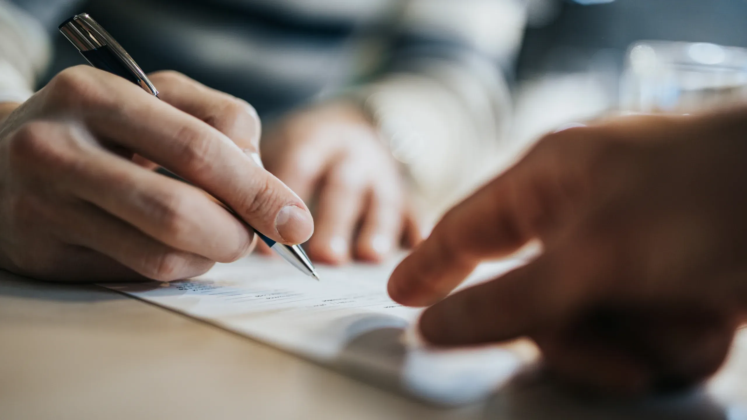 Person signing a document, completing paperwork in a professional business setting. 