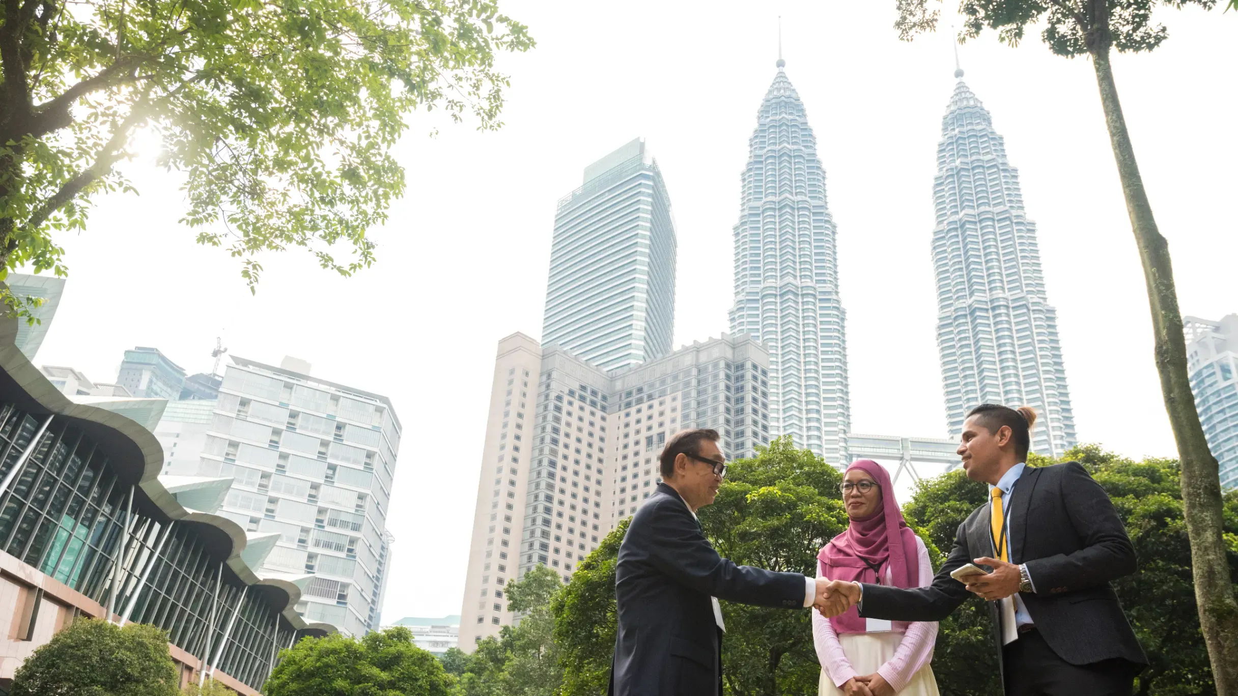 Business team having an outdoor meeting in Kuala Lumpur, collaborating in a professional setting with the city skyline nearby. 