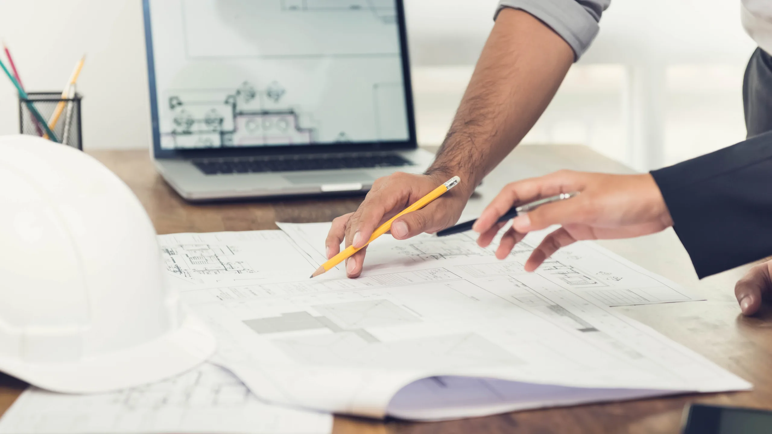 Colleagues discussing a building project at a desk, reviewing plans and collaborating on development proposals. 