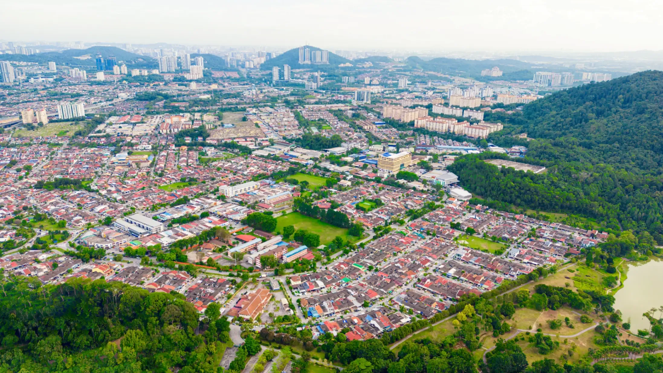 Drone view of a suburban neighbourhood showing residential streets, homes, green spaces, and surrounding infrastructure. 