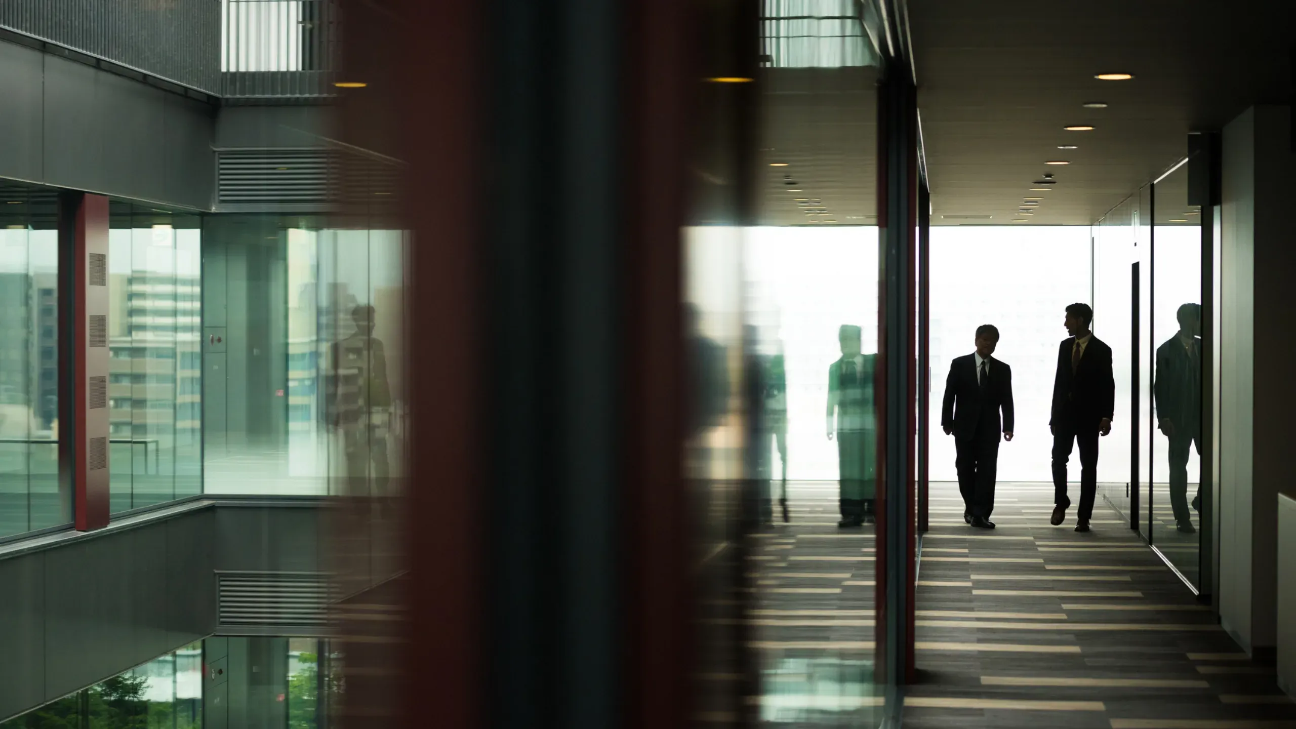 Two colleagues discussing business in a modern office corridor with contemporary interior design and glass partitions. 