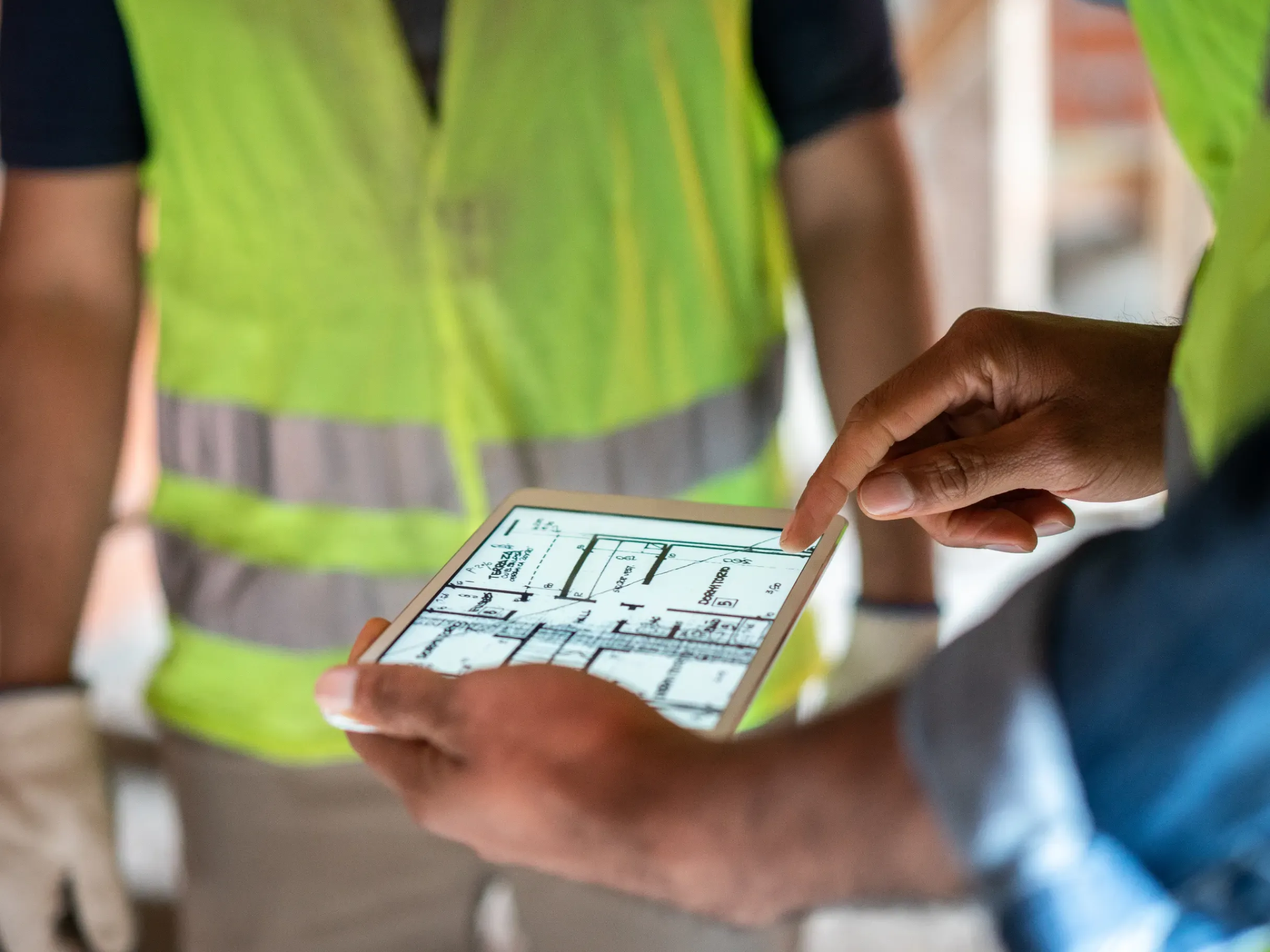 Construction site engineer reviewing project plans on a digital tablet while overseeing development work. 