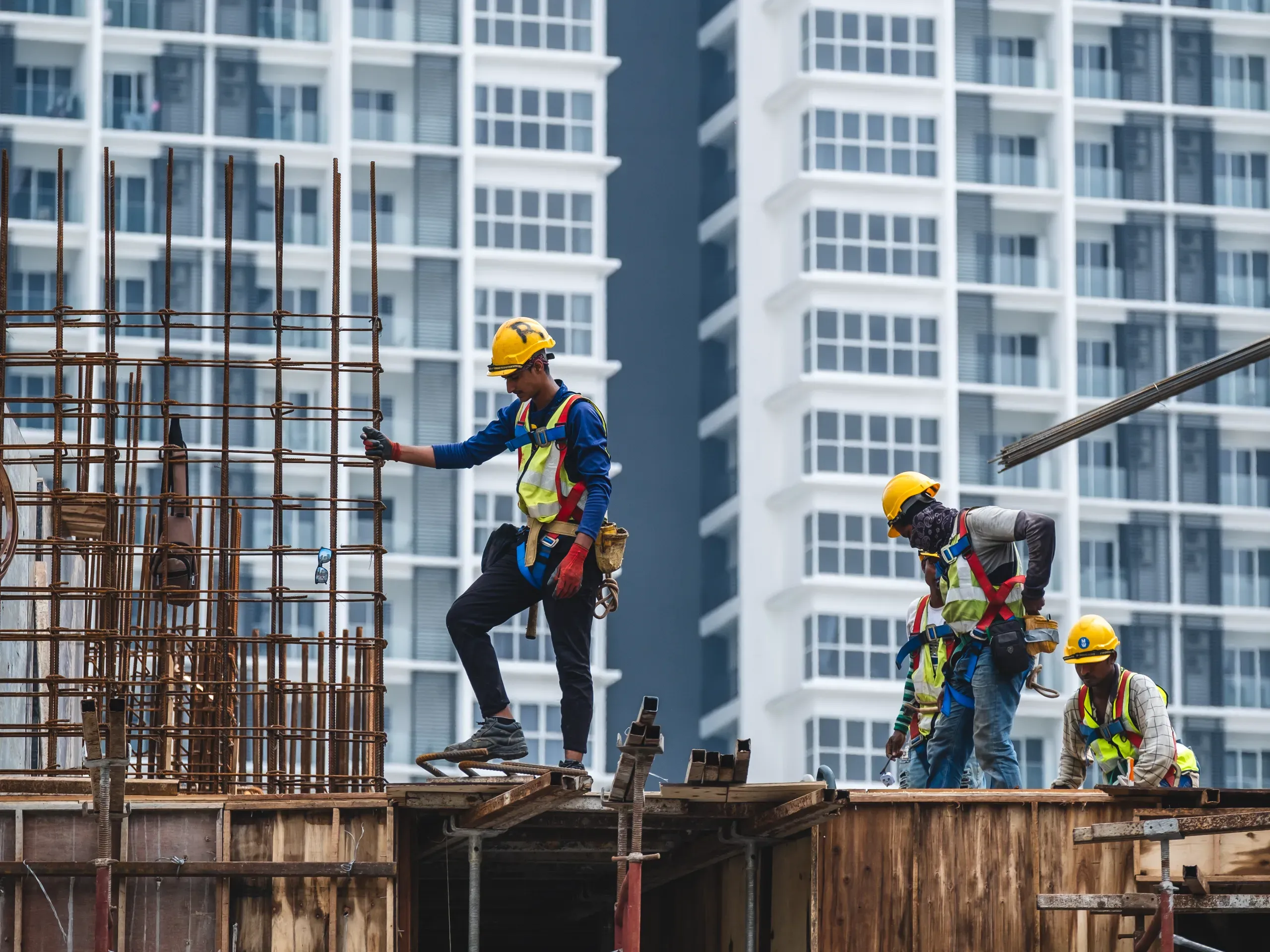 Construction workers wearing safety equipment while working on a high-rise building development site. 