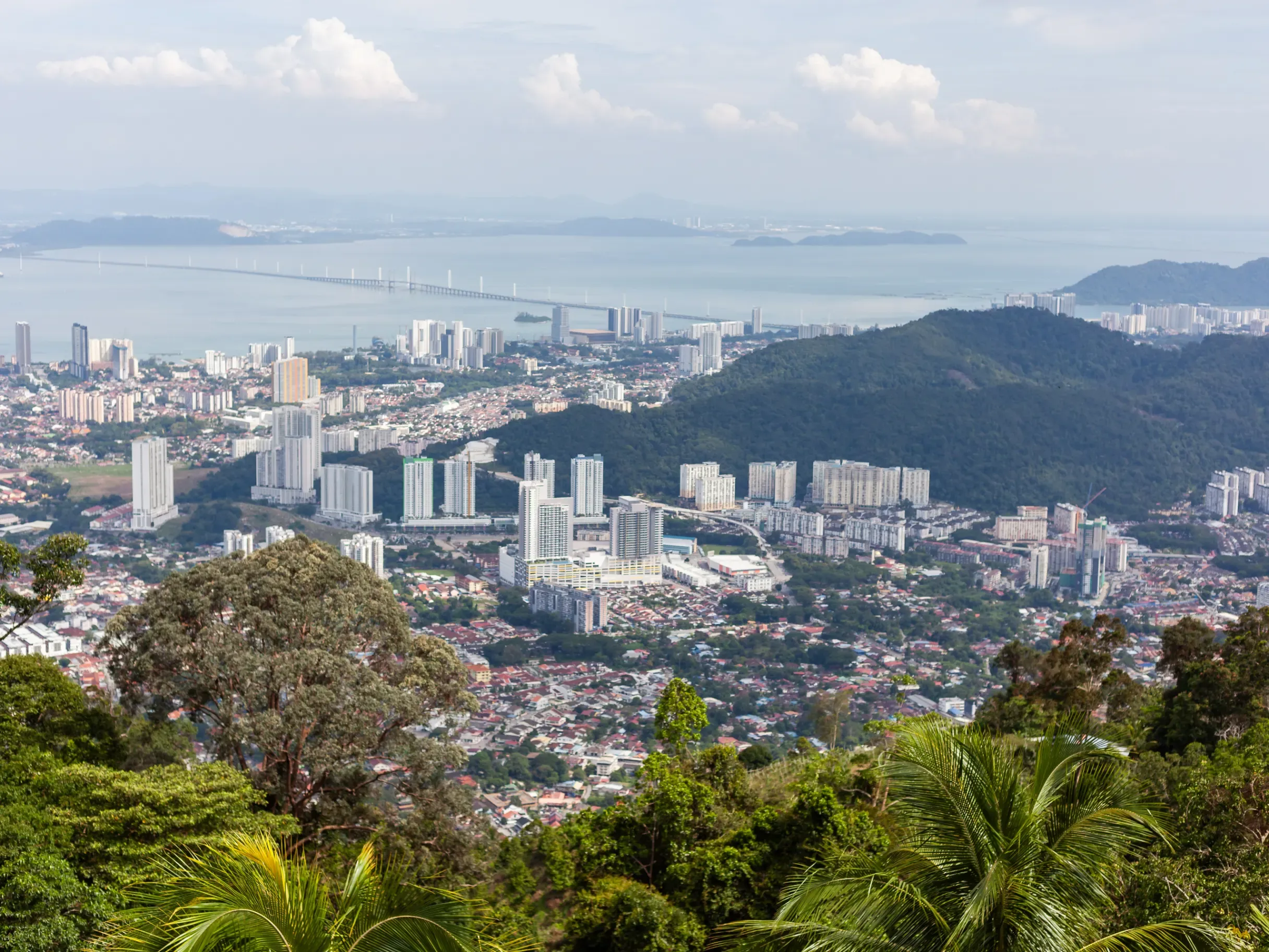 Malaysian cityscape set against lush green hills, combining urban development with natural surroundings. 