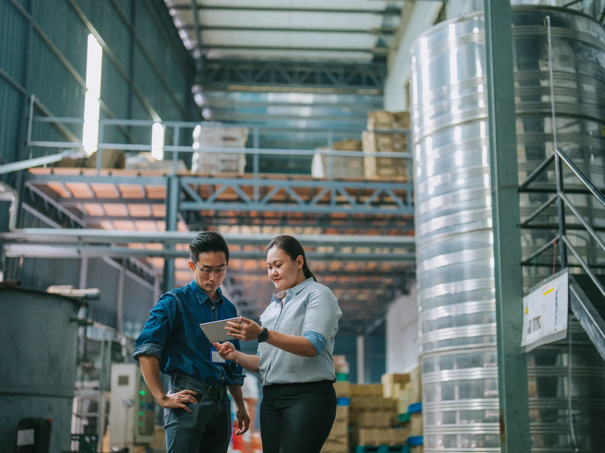 Manager speaking with a warehouse foreperson inside a factory, reviewing operations and workflow. 