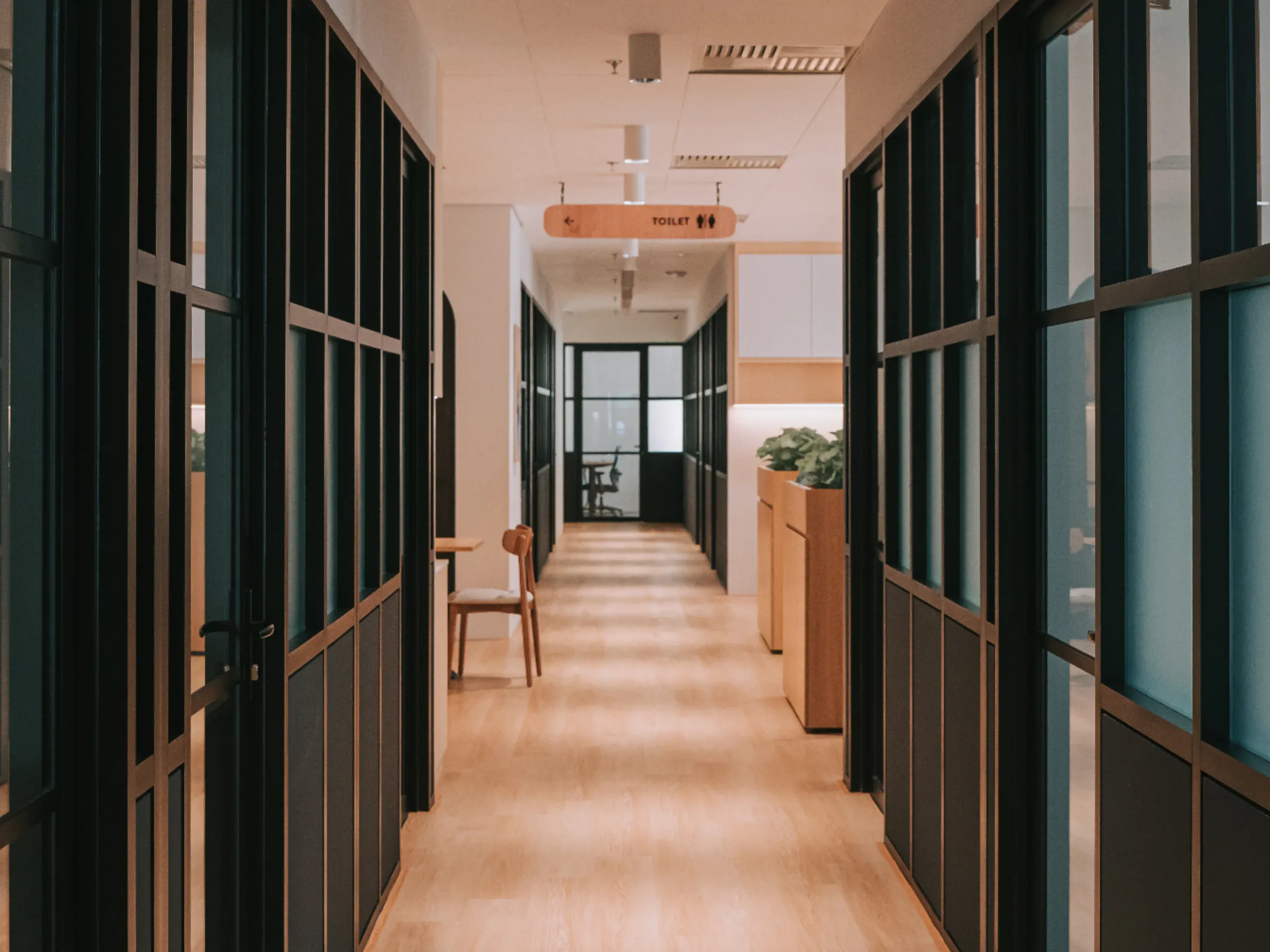 Modern office corridor with glass partitions, wooden flooring, and a bright, contemporary interior design