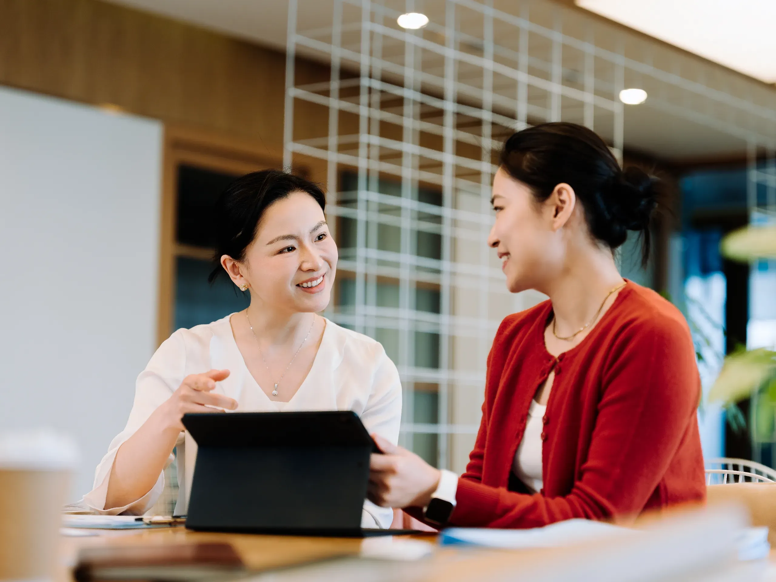 two Asian businesswomen working together on a computer, collaborating on tasks in a professional office setting. 