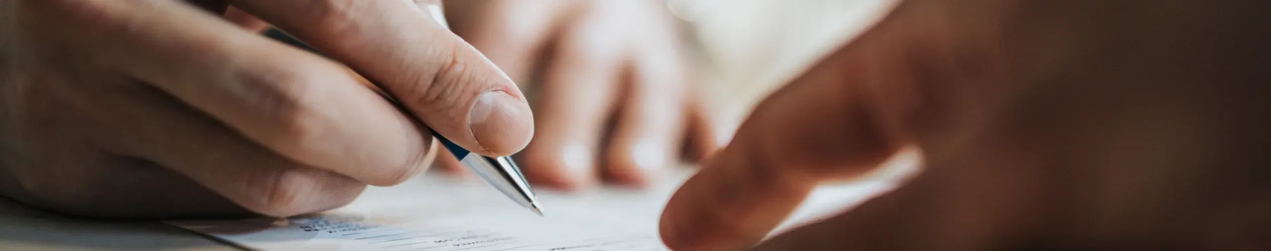 Person signing a document, completing paperwork in a professional business setting. 