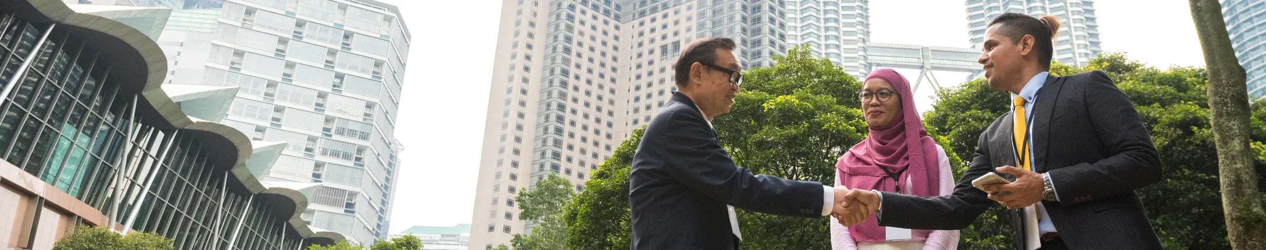 Business team having an outdoor meeting in Kuala Lumpur, collaborating in a professional setting with the city skyline nearby. 