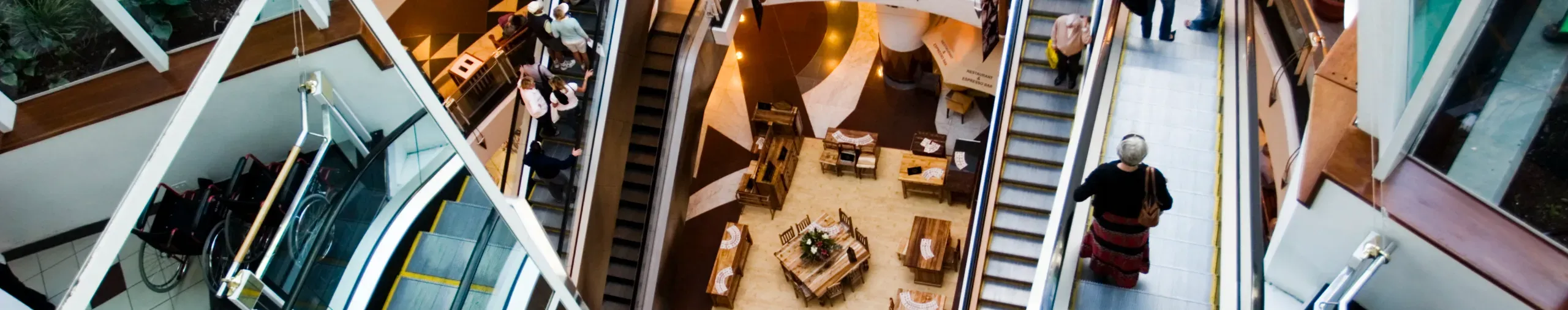 Overhead view of a shopping mall interior, showing retail spaces, walkways, and open communal areas. banner