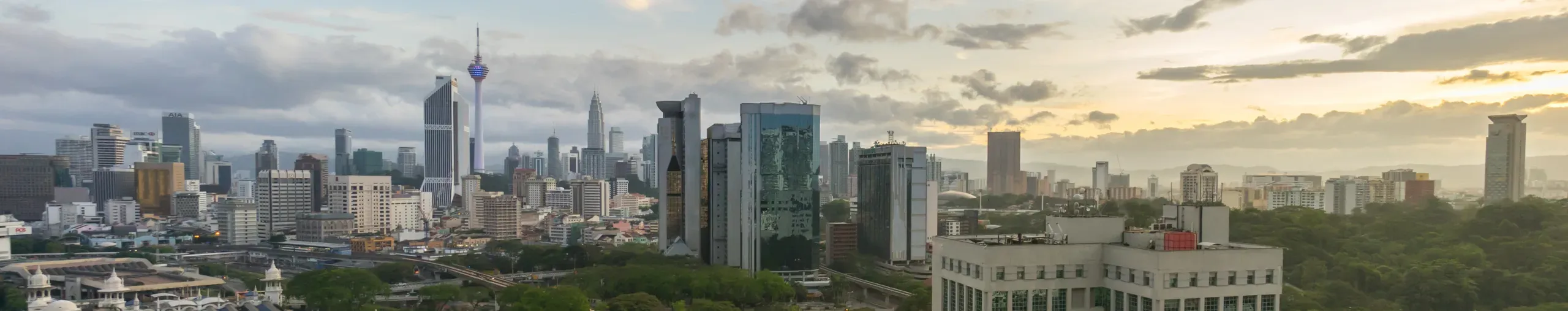 Sunrise over Kuala Lumpur with the city skyline illuminated by soft morning light and a colourful dawn sky banner