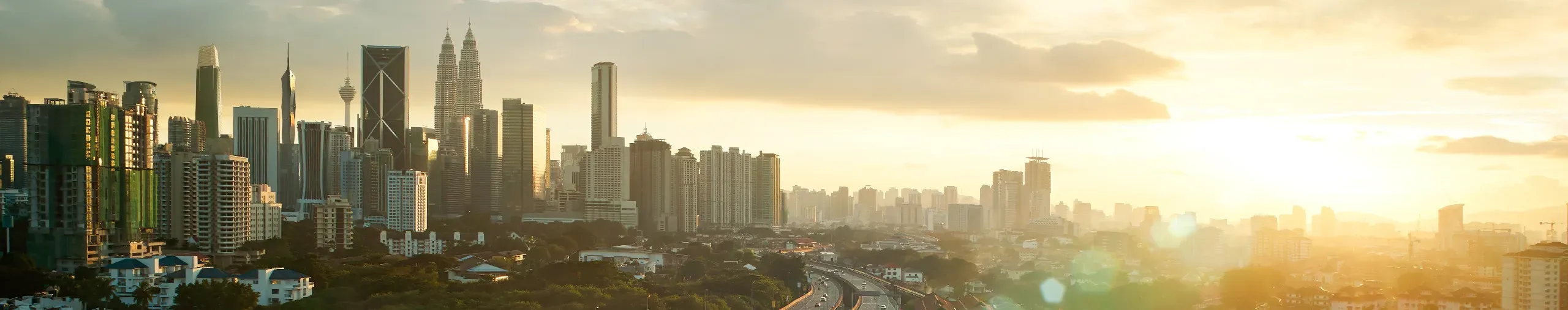 Sunset over Kuala Lumpur, with the city skyline silhouetted against a warm, colourful evening sky - banner